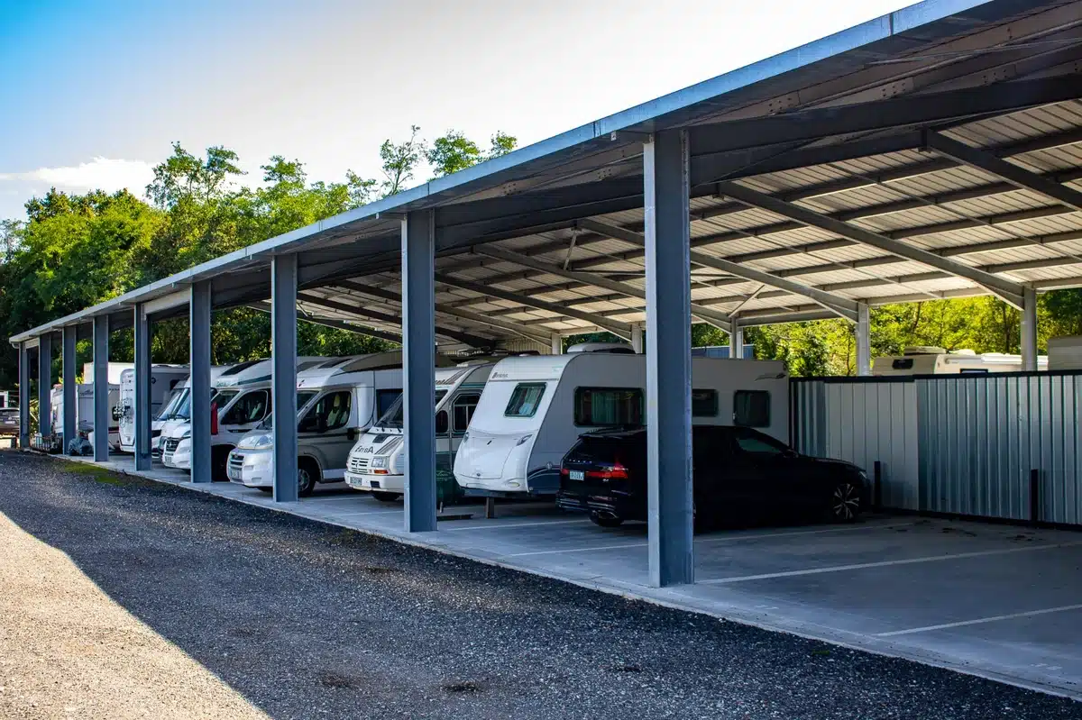 Grand abri métallique pour camping-cars, caravanes et voitures stationnés en rangées. Un espace de stockage extérieur sous un ciel bleu.