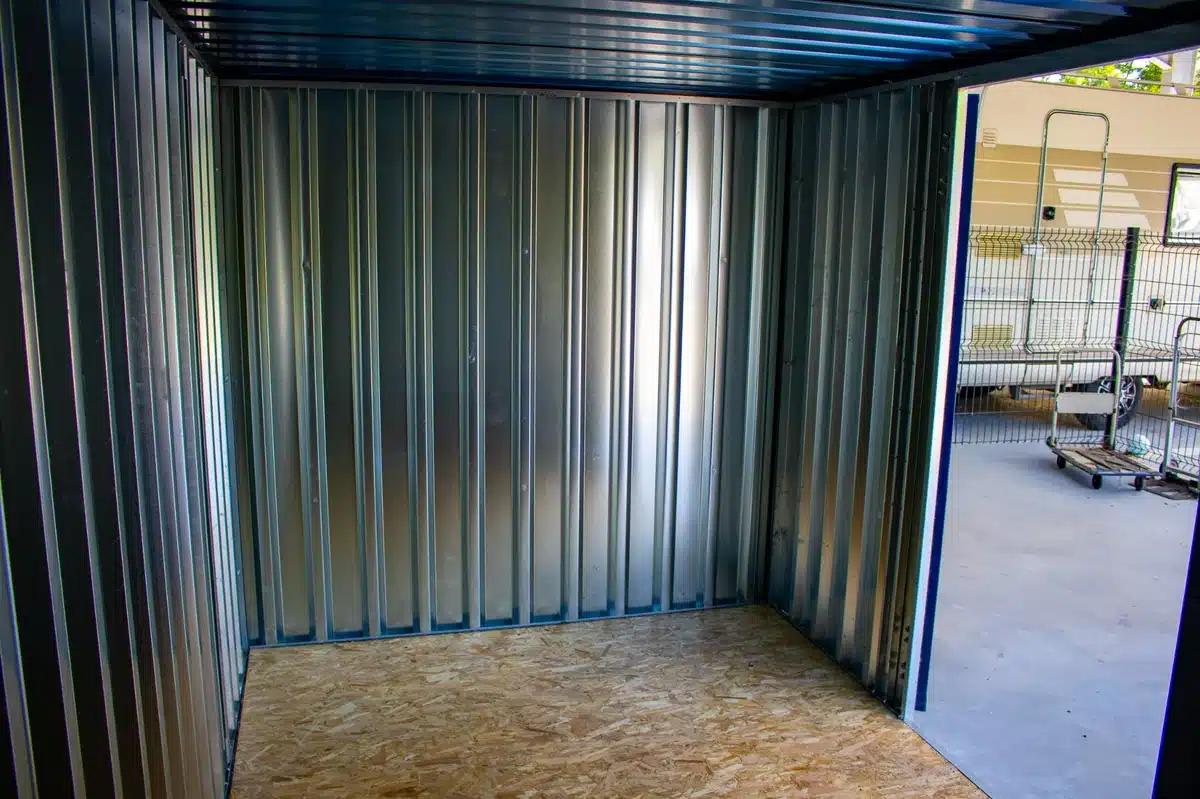 Box de self-stockage vide, intérieur métallique et plancher en bois. Porte ouverte sur l'extérieur avec un camping-car.