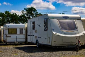 Deux caravanes blanches, dont une Caravelair Osiris 516, garées sur gravier sous un ciel bleu nuageux avec des pins.