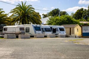 Caravanes garées sur un parking ensoleillé, bordé de palmiers. Panneau de services PALACE P: Gardiennage, Réparations, Remorquage.
