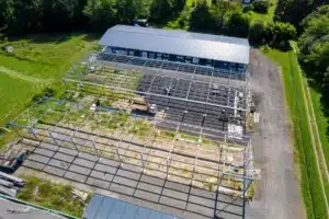 Vue aérienne d'un chantier : structure métallique de hangar en construction près d'un bâtiment abritant des camping-cars, sur un terrain verdoyant.