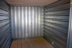 Intérieur vide d'un conteneur de stockage avec murs en tôle ondulée métallique et sol en bois clair. Un autocollant indique « THIS SIDE DOWN ».