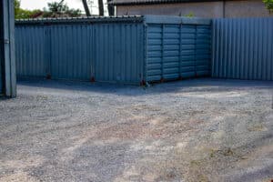 Conteneurs de stockage métalliques gris avec portes et panneaux texturés, alignés sur un sol en gravier. Le numéro 52 est visible.