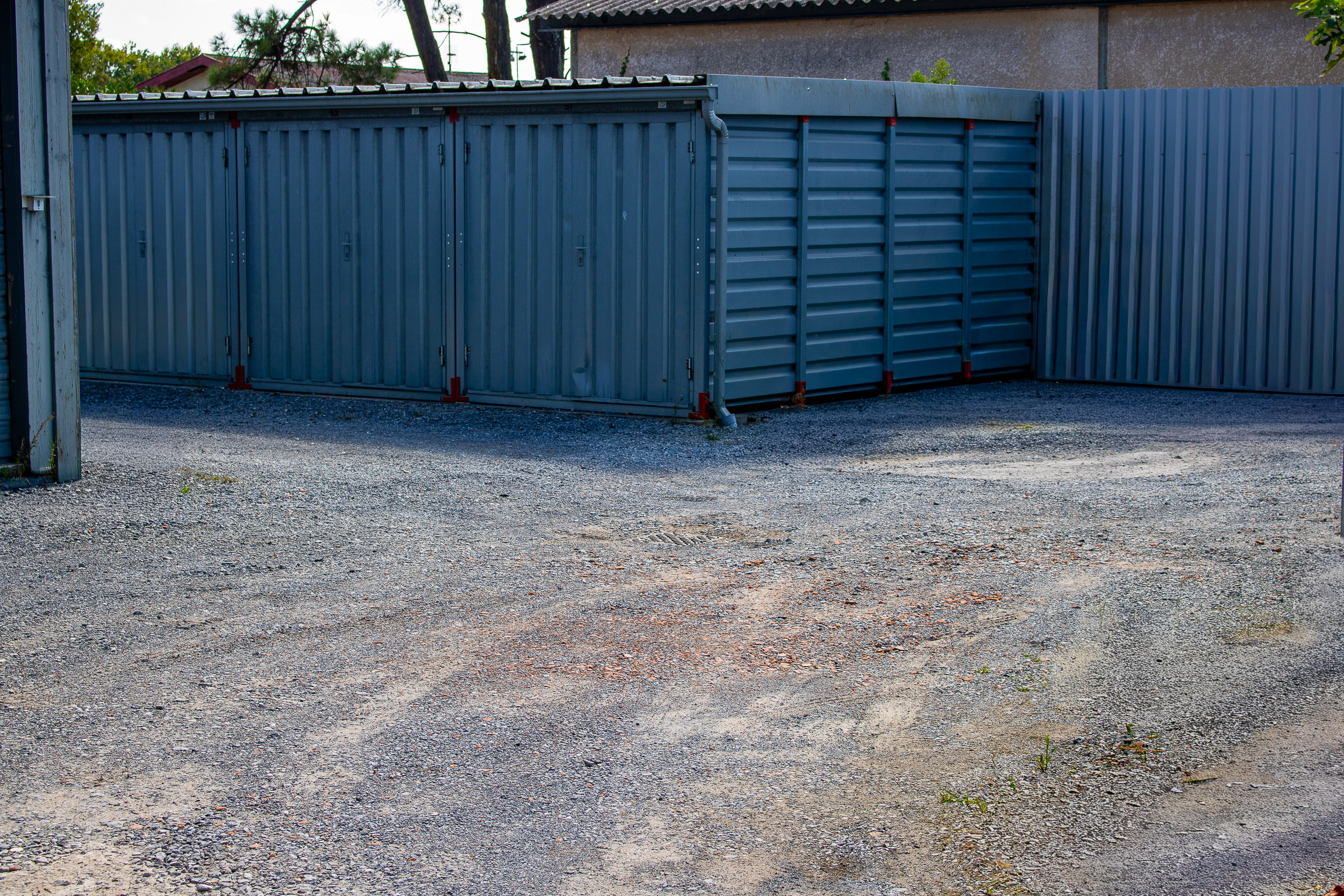 Conteneurs de stockage métalliques gris avec portes et panneaux texturés, alignés sur un sol en gravier. Le numéro 52 est visible.