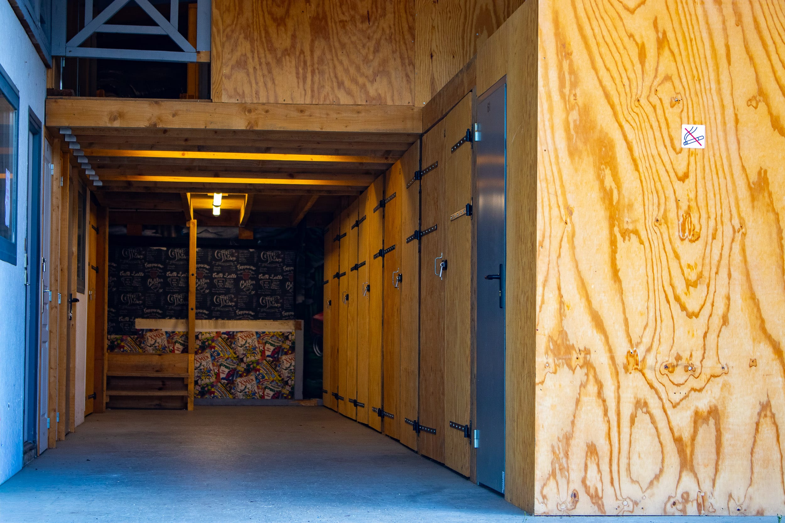 Passage intérieur en bois avec casiers, décor mural Coffee Shop, X-Men, et panneau "interdit de fumer". Porte numéro 61 visible.