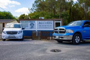 Un van Mercedes blanc et un pick-up RAM bleu devant les panneaux Palace Park affichant accueil, gardiennage, réparations, remorquage et coordonnées de contact.