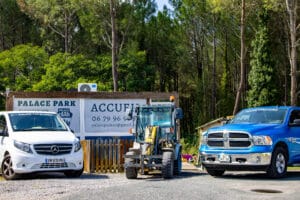 Van Mercedes blanc, chargeur jaune et pick-up Ram bleu devant un panneau Palace Park et la forêt. Infos: Accufi, palacepark40@gmail.com.