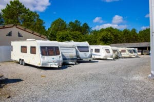 Caravanes blanches de marques Bailey, Fendt et Hobby garées en rang sur un parking extérieur en gravier sous un ciel bleu clair.