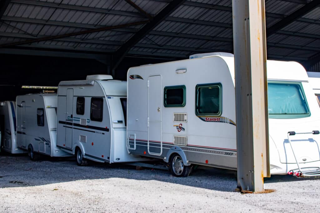 Plusieurs caravanes blanches, dont une Starlett 390CP et une Avia 3900, sont stationnées sous un abri métallique sur gravier.