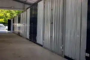 Rangée d'unités de stockage en métal galvanisé et noir sous un abri. Une porte est ouverte, montrant des arbres en arrière-plan.